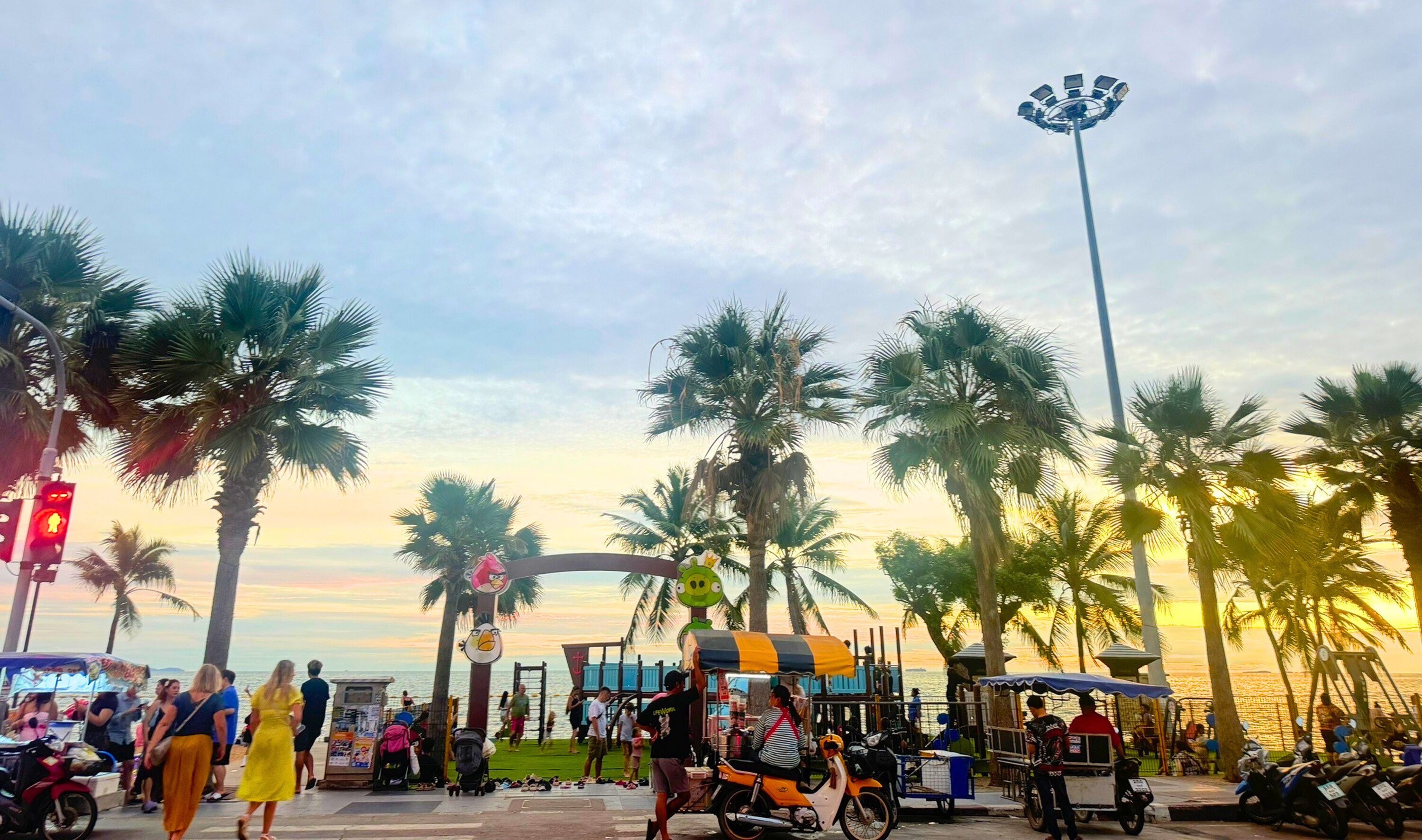 A busy coastal promenade with palm trees, street vendors, and people walking.