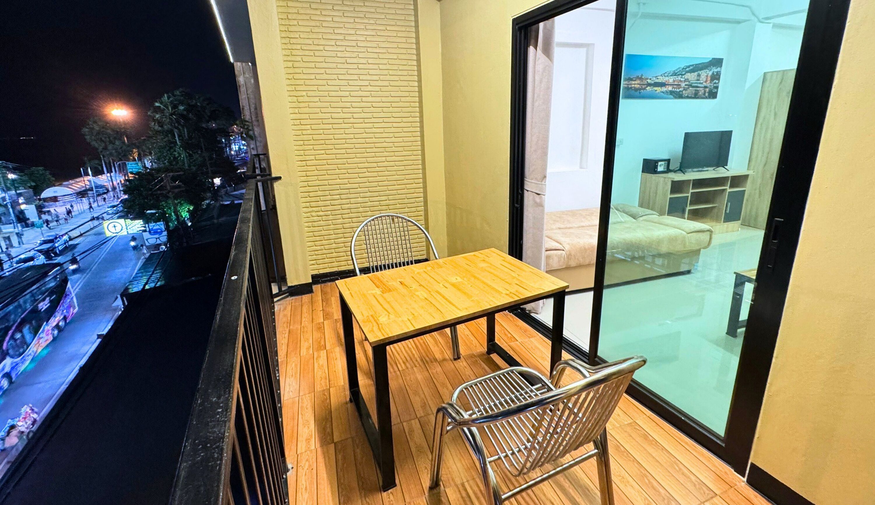A balcony with a wooden table and chairs, a city view, and a glass door leading to a living area.