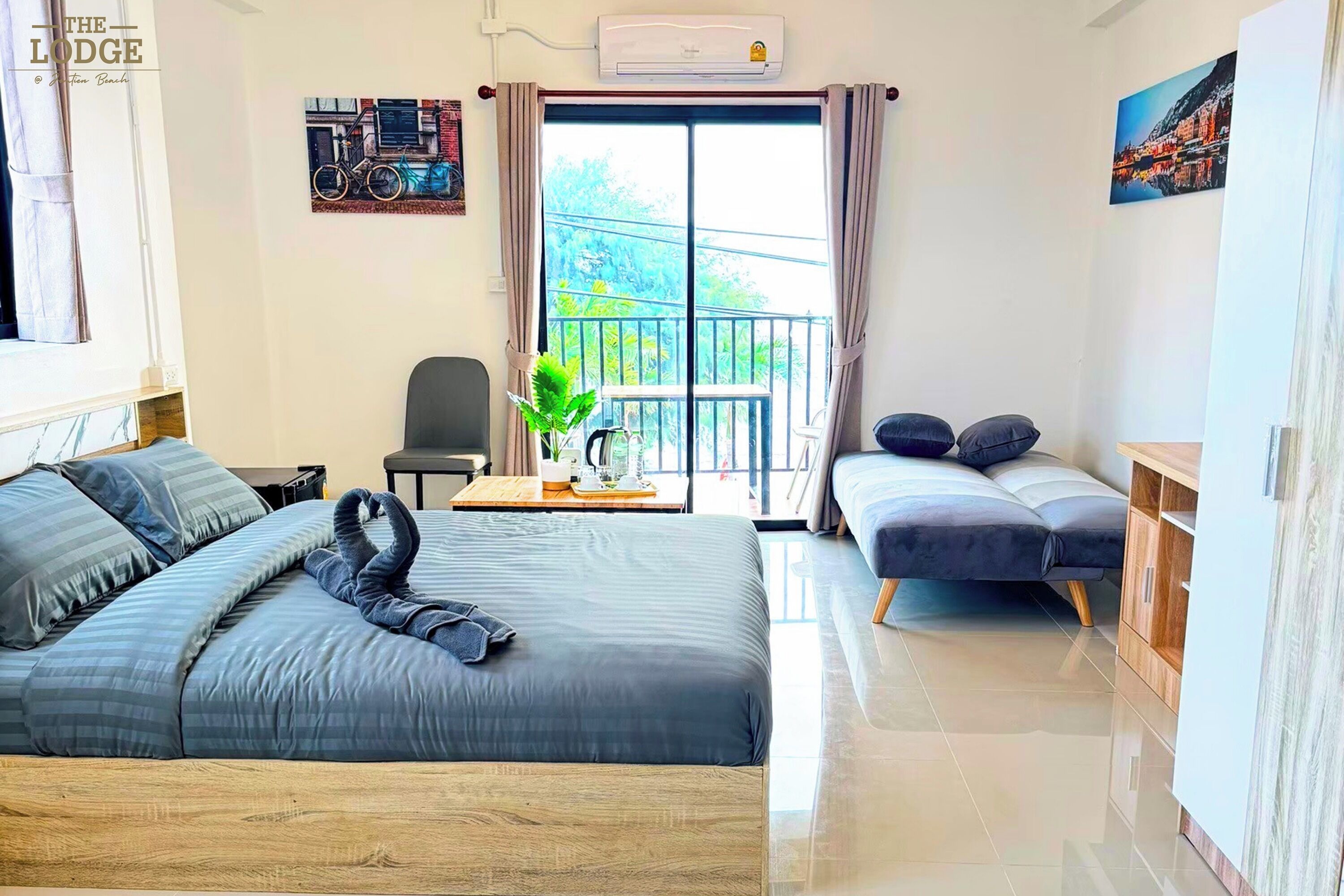 Ein Hotelzimmer mit Bett, einer Couch, einem kleinen Tisch mit Pflanze und einem Balkon mit Geländer.