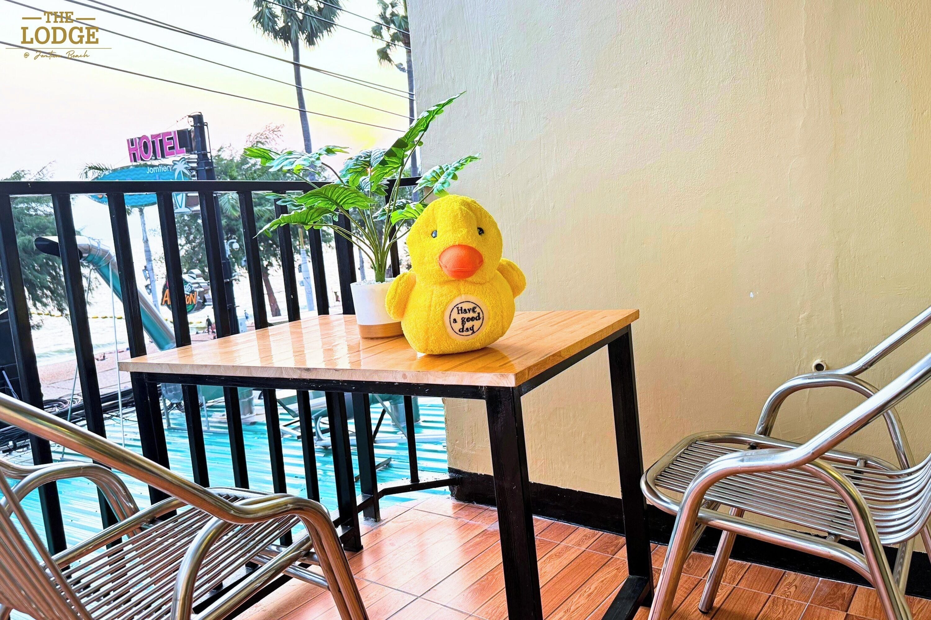 Um brinquedo de pato amarelo de pelúcia sobre uma mesa de madeira, com uma cadeira de metal ao lado, com vista para uma área de piscina.
