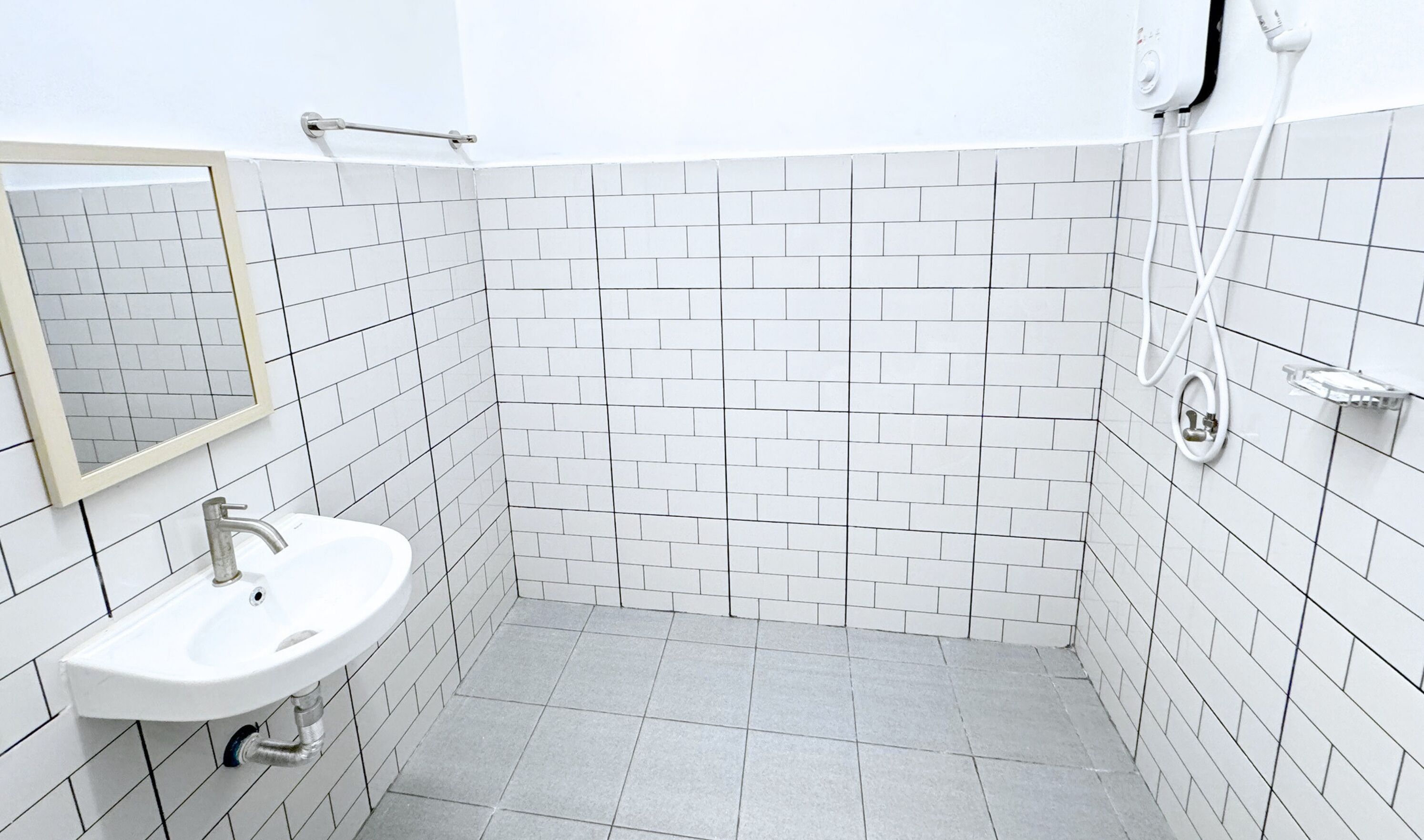 A small, modern bathroom with white tiles, a sink, a mirror, and a handheld showerhead.