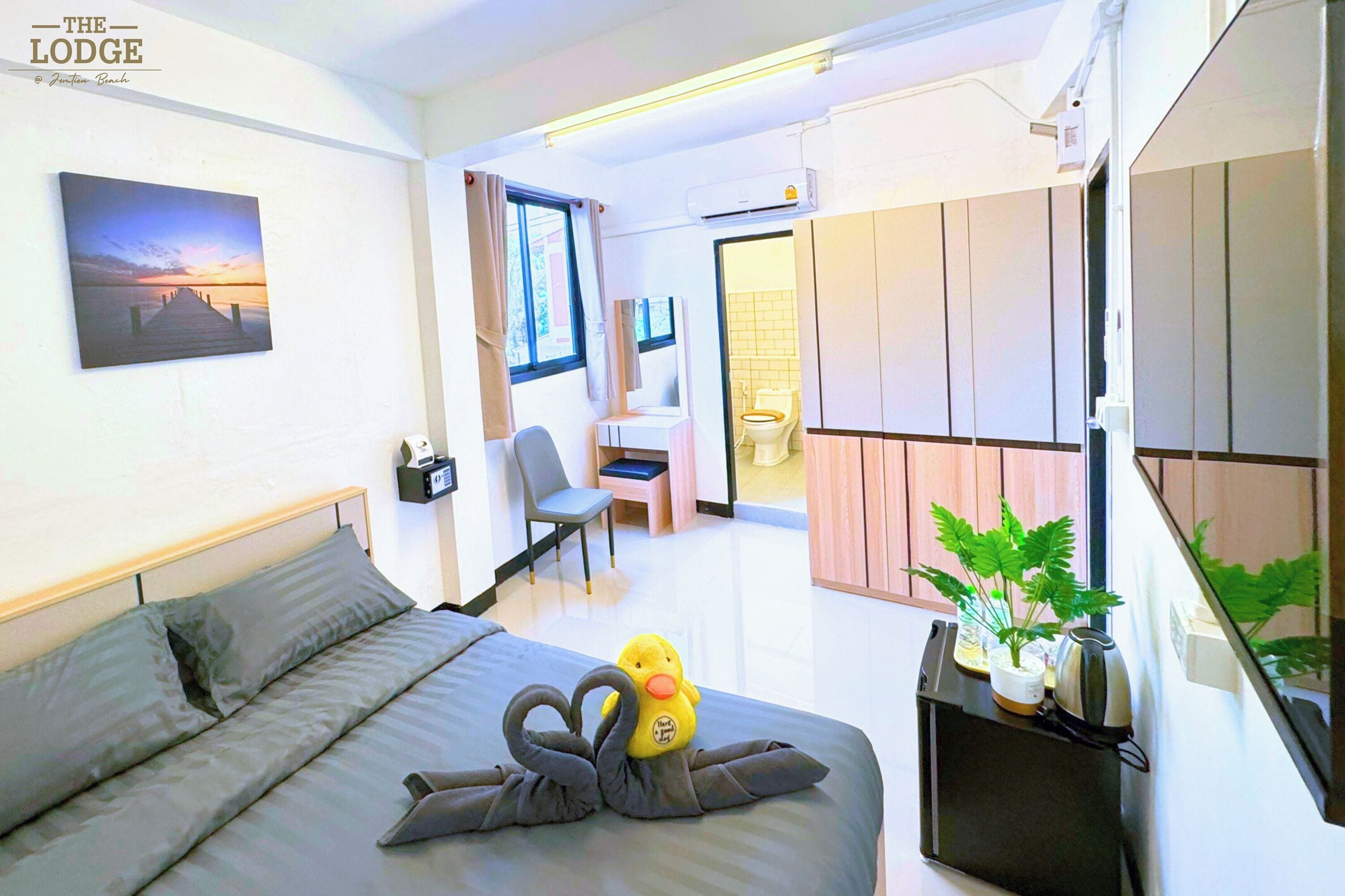 A modern hotel room with a bed, a desk, a chair, a potted plant, and a view of the outside.