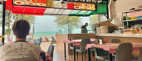 Un restaurante con terraza al aire libre y vistas al mar, con un chef preparando comida en la barra.