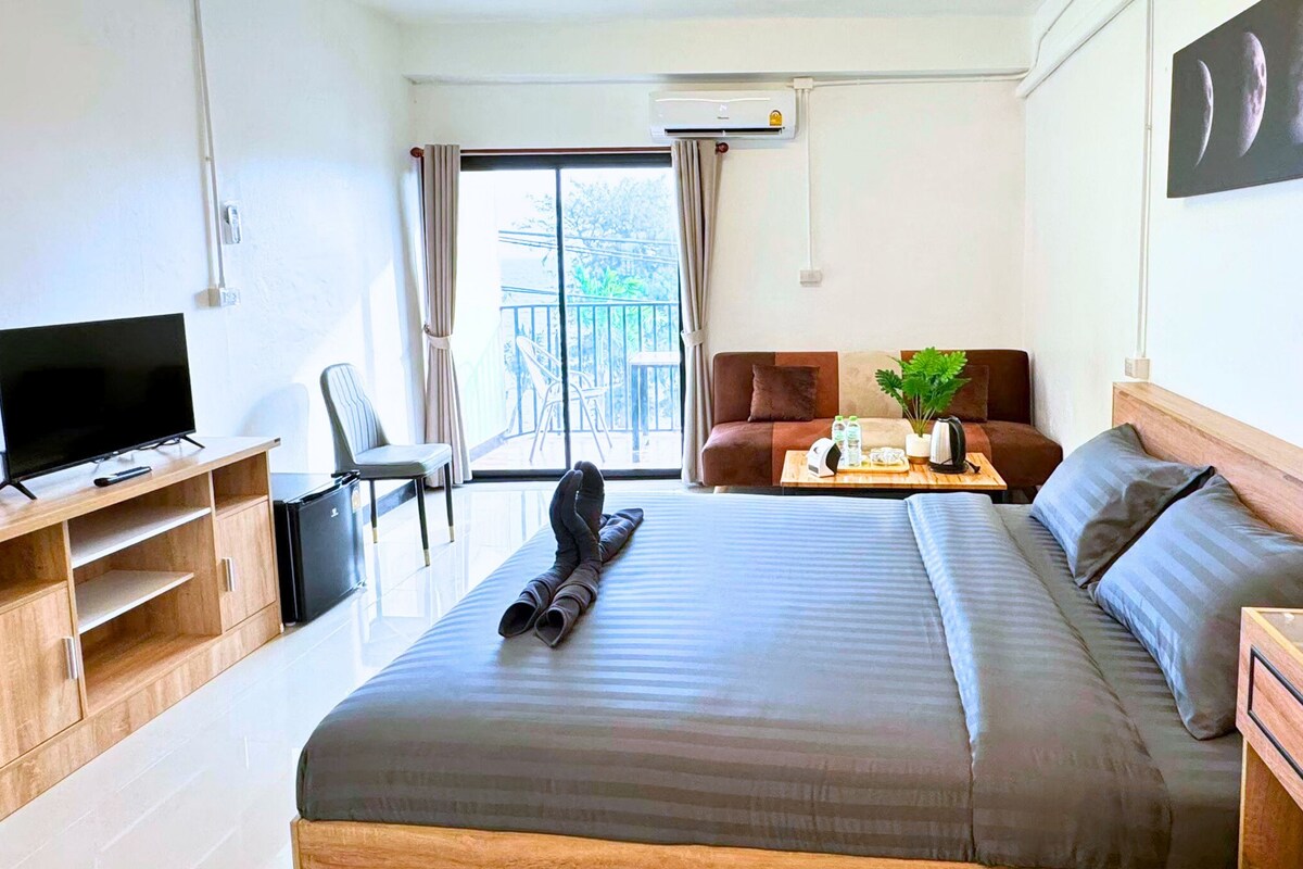 Habitación de hotel con cama, televisión, sofá, mesa de centro y balcón con vistas.