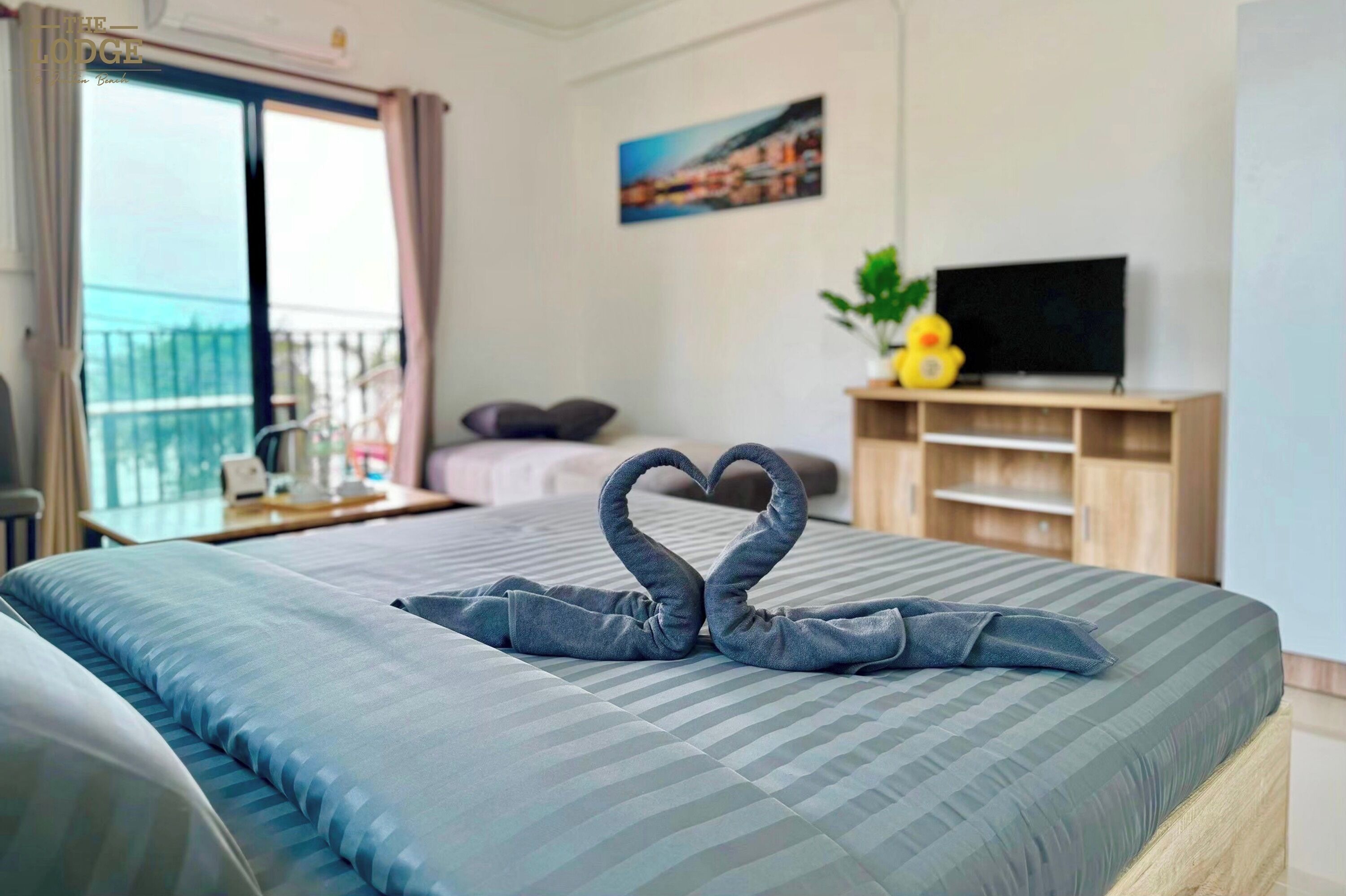 A hotel room with a bed, a TV, a plant, and a balcony with a view.
