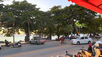 Vista da rua com veículos estacionados, incluindo carros e motocicletas, e algumas pessoas caminhando.