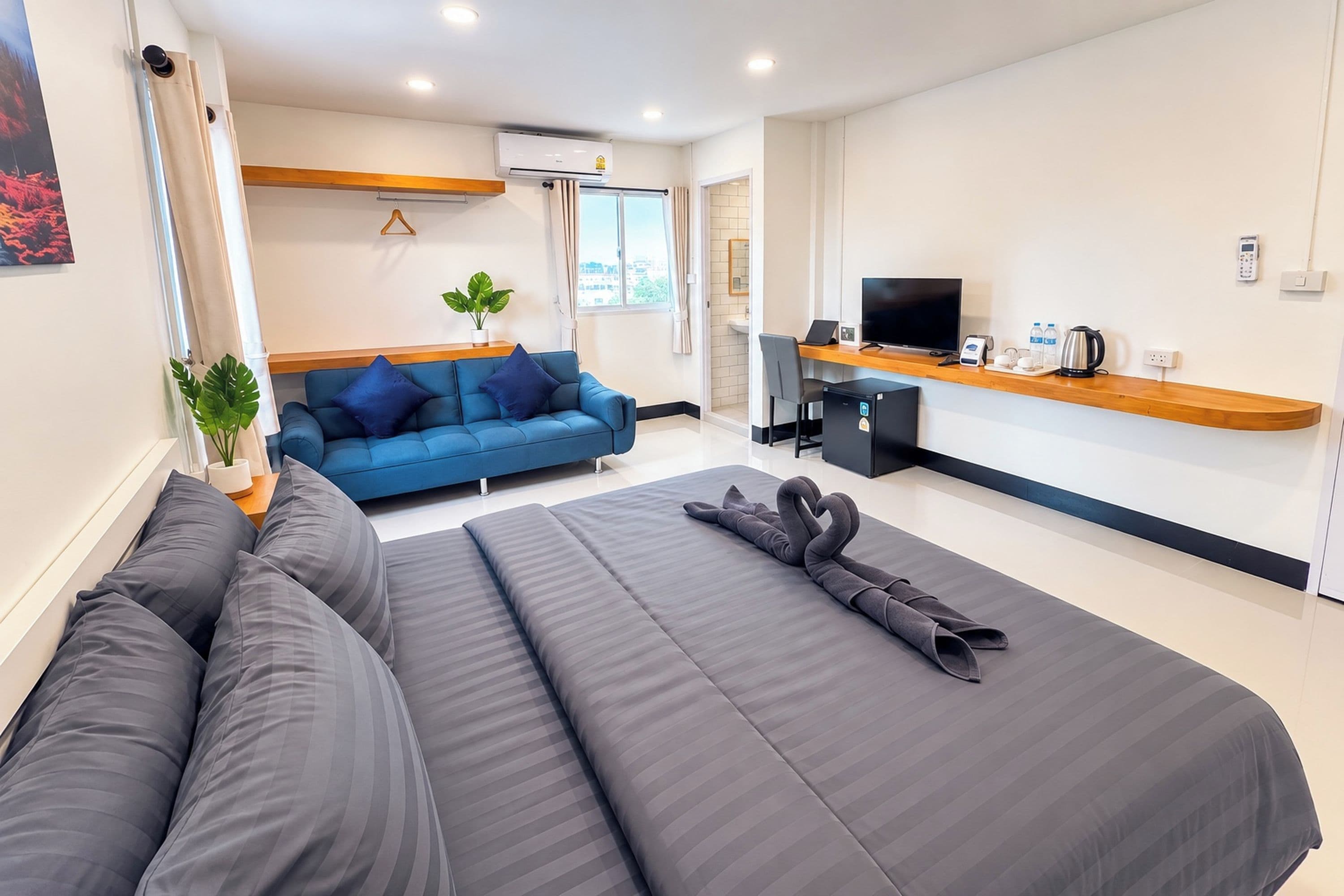 A modern hotel room with a large bed, a sofa, a desk with a computer, and a TV.