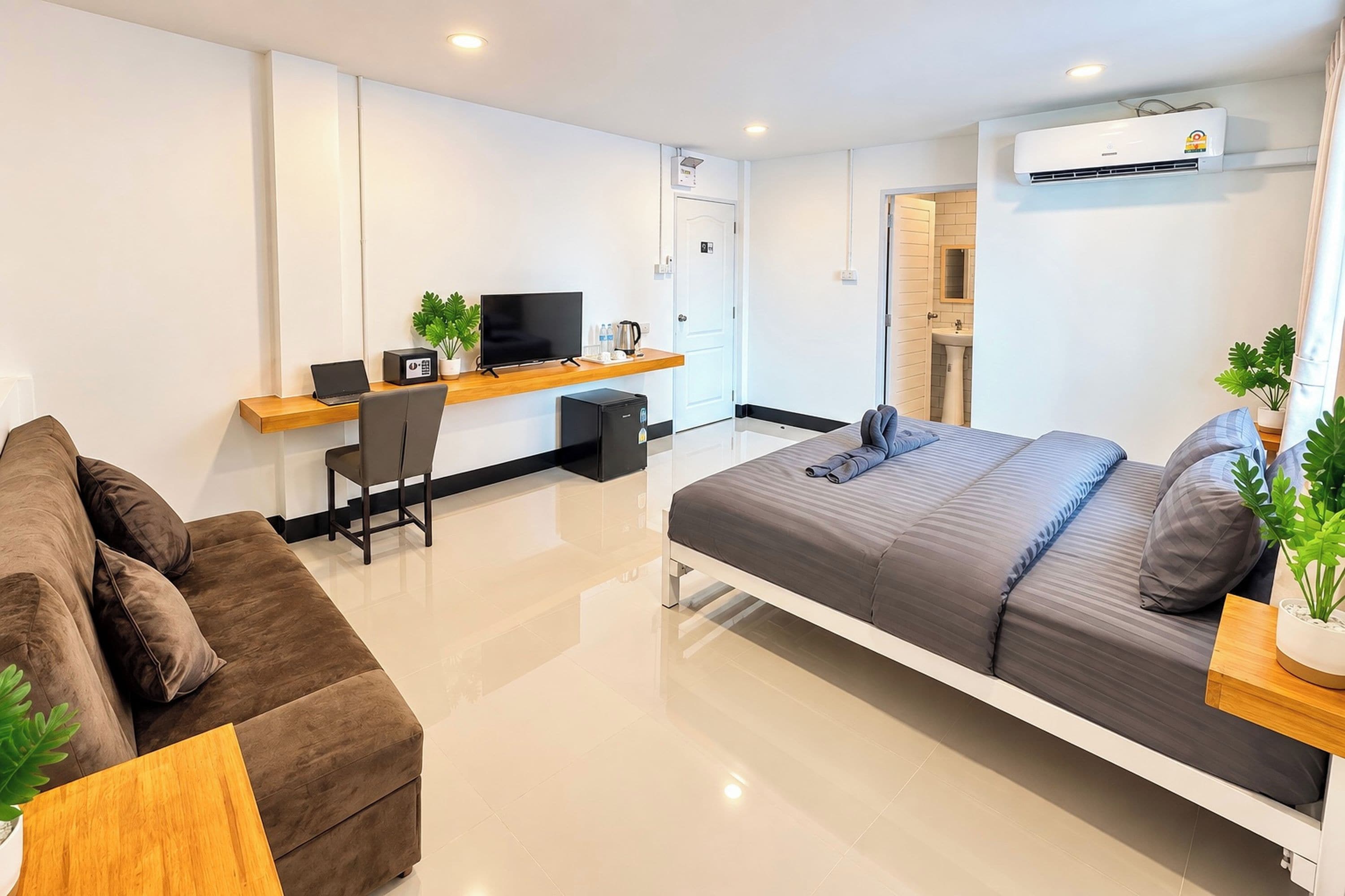 A modern hotel room with a bed, a desk, a chair, a sofa, and an air conditioning unit.