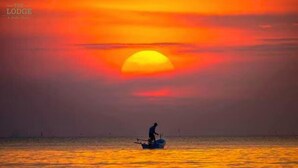 Un coucher de soleil sur une mer calme, avec un seul bateau et une personne à bord.