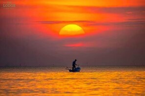 Ein Sonnenuntergang über einem ruhigen Meer mit einem einzelnen Boot und einer Person darin.