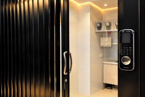 A modern bathroom with a sleek design, featuring a black door with a metallic handle, a digital lock, and a control panel with a keypad and a circular button. - The Lodge Jomtien 9 (Pattaya)