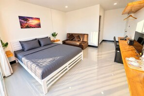 Ein modernes Schlafzimmer mit einem großen Bett, einer Couch, einem Schreibtisch mit Computer und einem Bild an der Wand.
