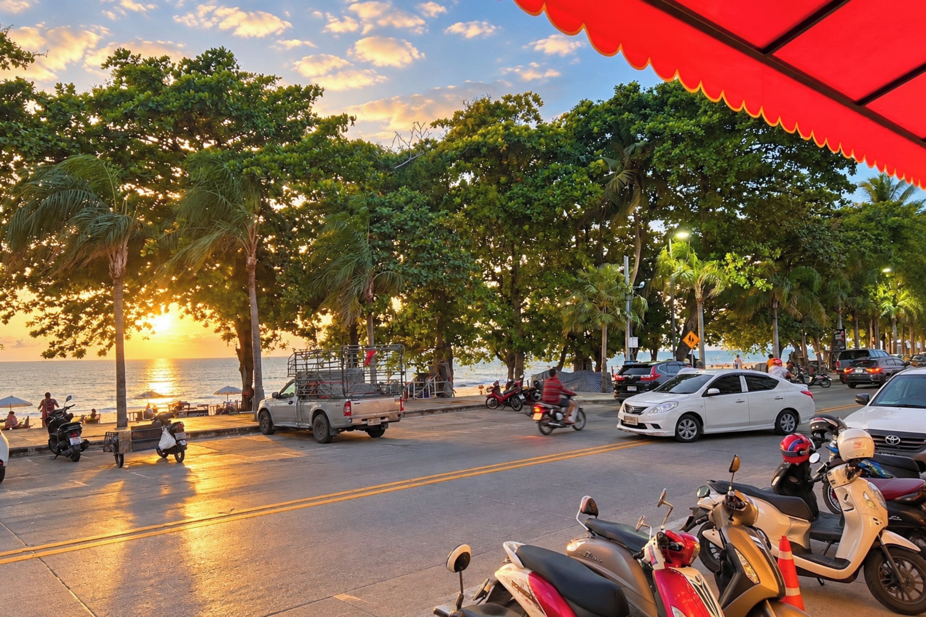 A coastal street lined with trees and parked vehicles, including scooters and cars, with a sunset in the background.