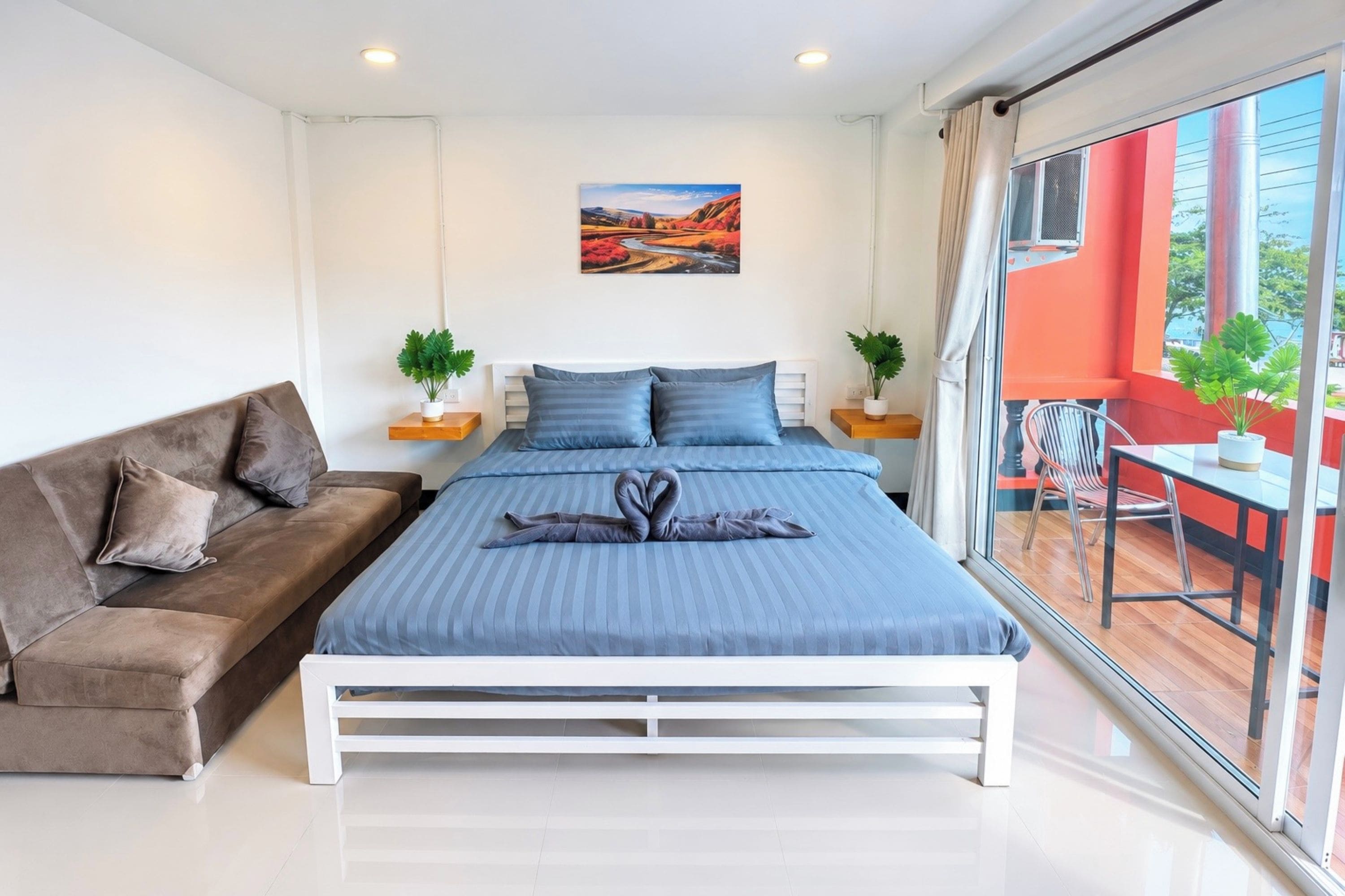 A modern bedroom with a bed, a sofa, two nightstands with plants, and a large window with a view.