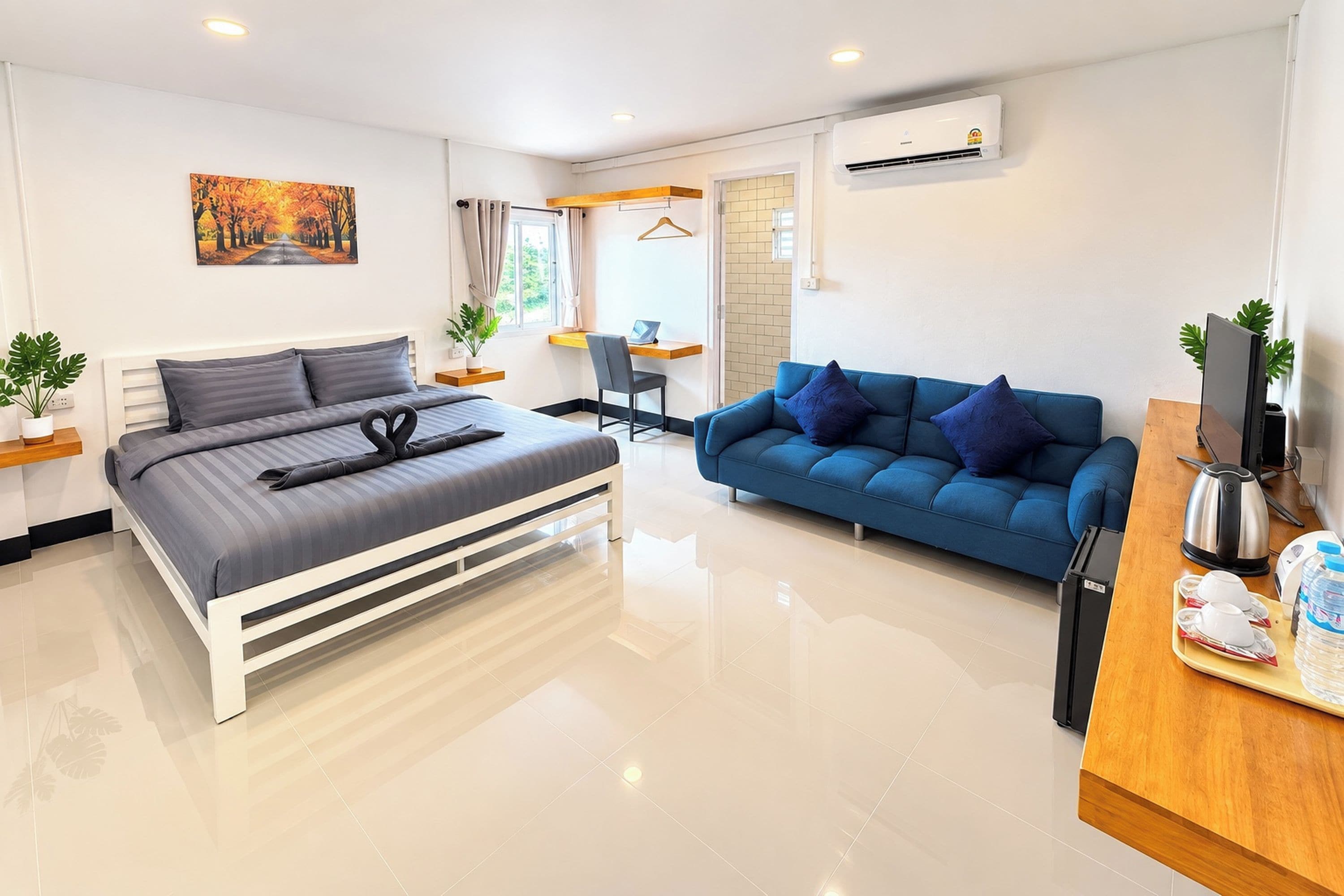 Habitación de hotel moderna con cama, sofá azul, escritorio con computadora portátil y cafetera.