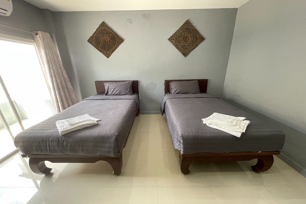 Quarto com duas camas, uma janela com cortinas e duas peças decorativas na parede.