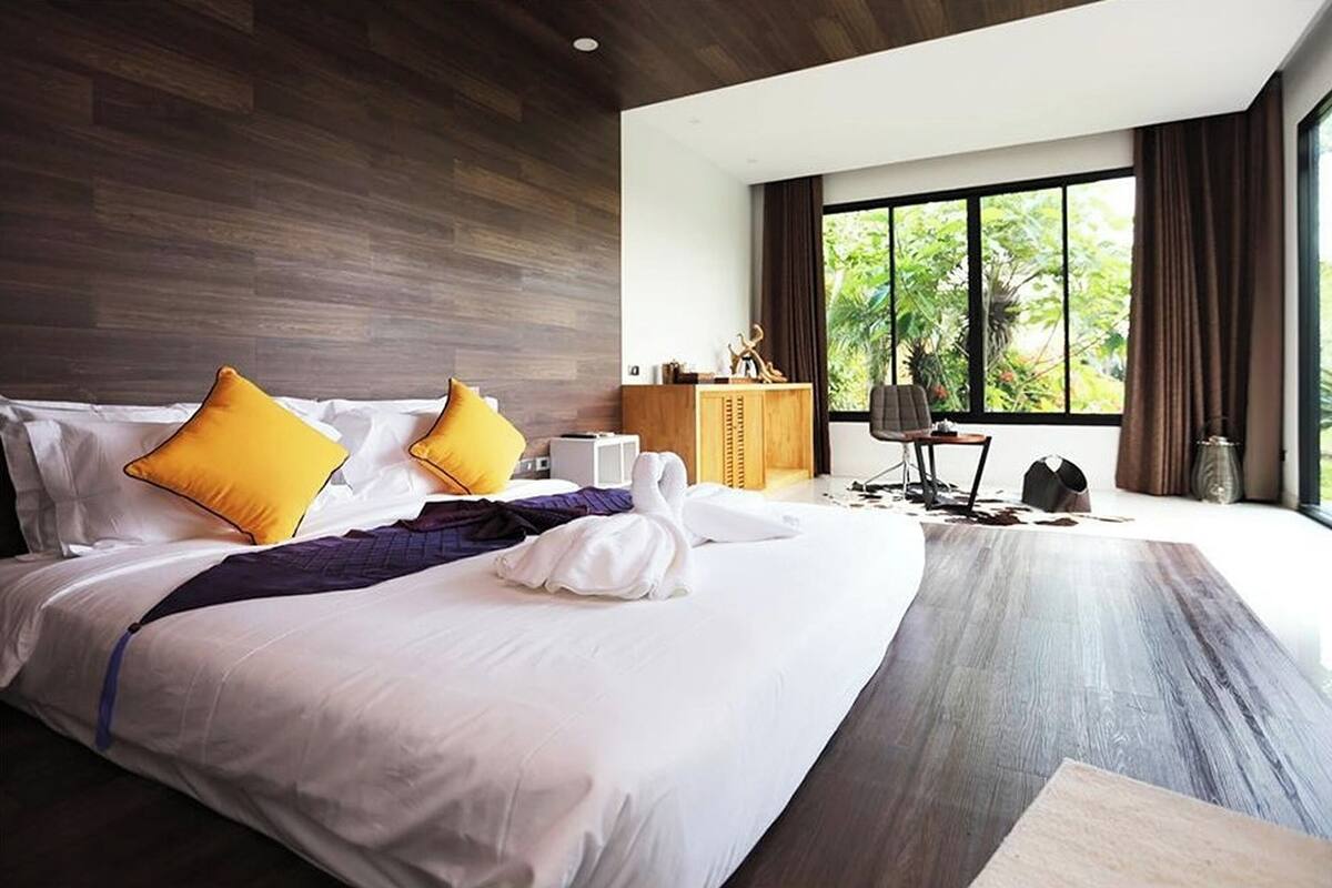 A modern hotel room with a large bed, wooden headboard, and a view of greenery outside.