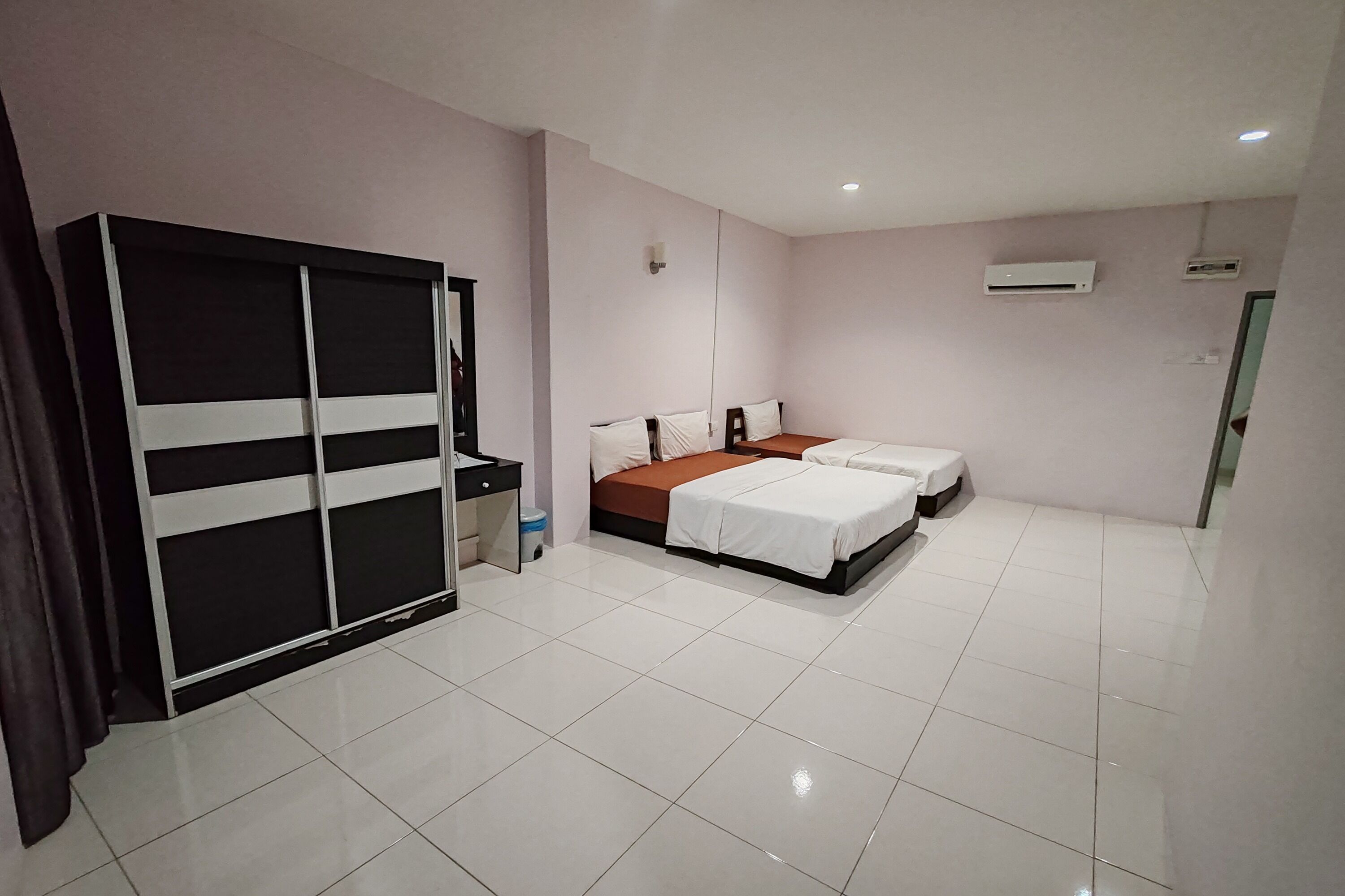 A hotel room with a large wardrobe, a bed with a brown mattress, and a white tiled floor.