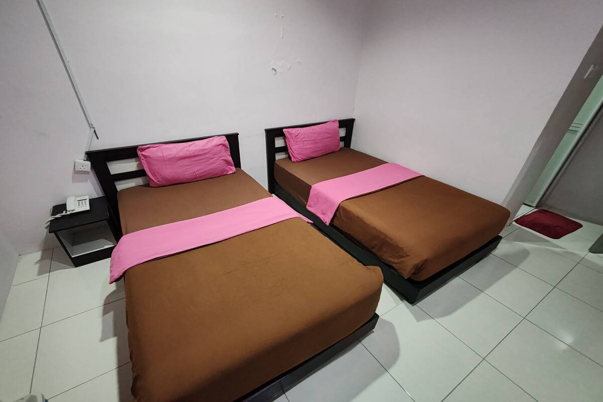 Two single beds with brown bedding and pink pillows in a room with white tiled floors.