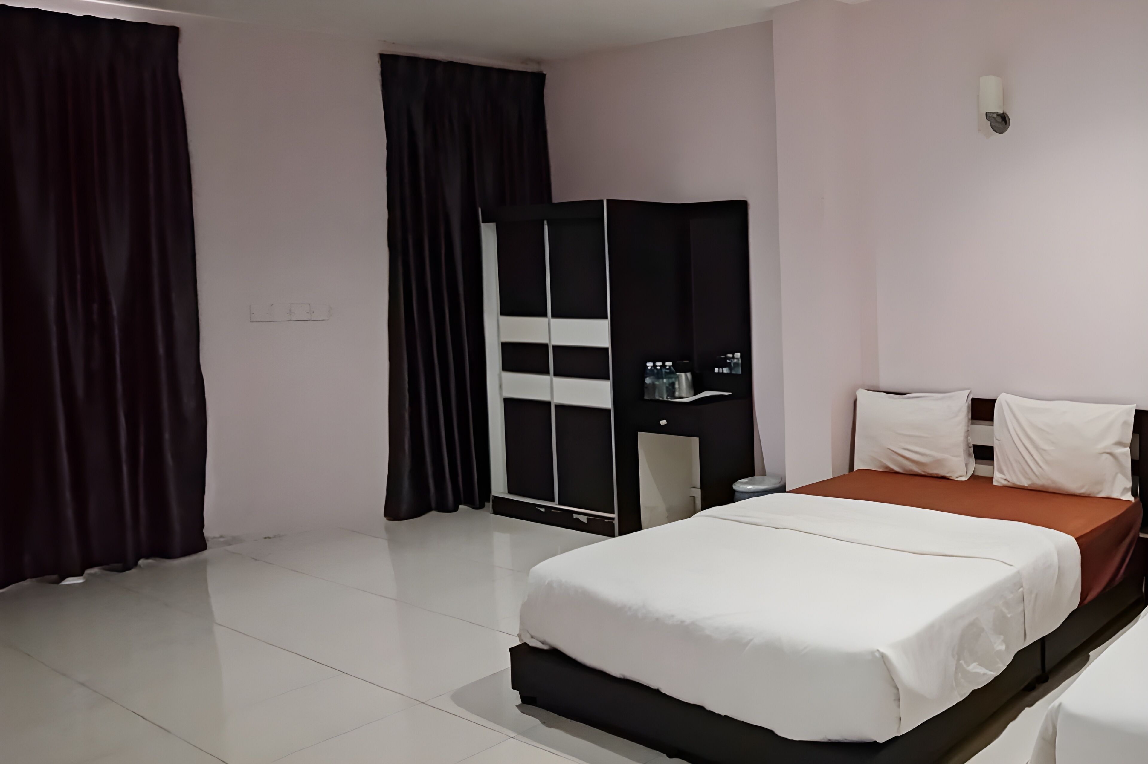 A hotel room with a bed, a wardrobe, a nightstand, and a wall-mounted light fixture.