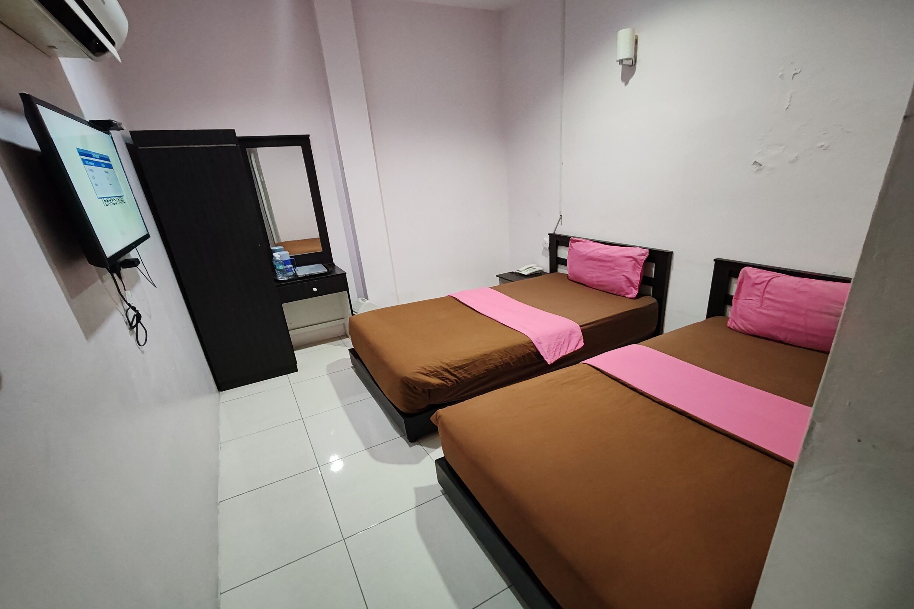 A hotel room with two beds, a TV, a desk, and a mirror.
