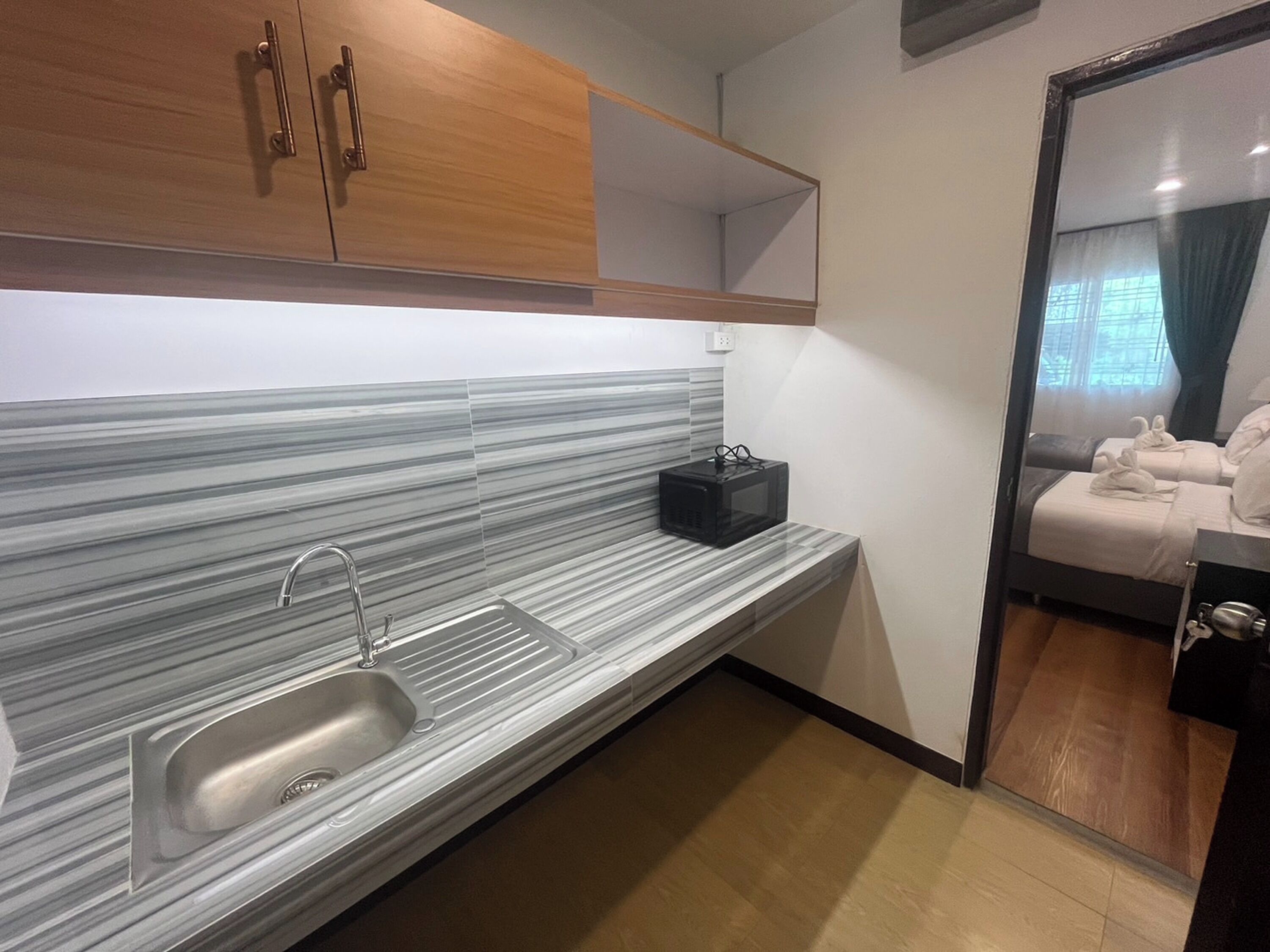 Une cuisine moderne dotée d’un évier en acier inoxydable, d’un four à micro-ondes et de meubles de rangement en bois.