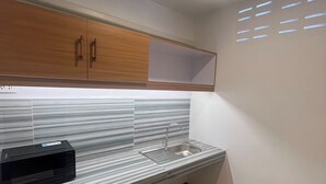 Uma cozinha moderna com micro-ondas embutido, pia de aço inoxidável e armários de madeira.