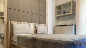 A modern bedroom with a wooden headboard, a bed with a grey blanket, a wooden nightstand, and a small cabinet with a mirror. - Sultan Residence Syariah (Jakarta)
