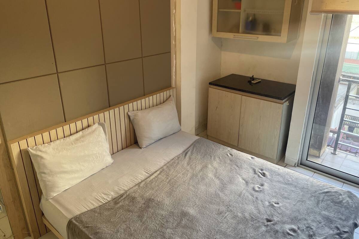 A bedroom with a bed, a small wooden cabinet, and a window.