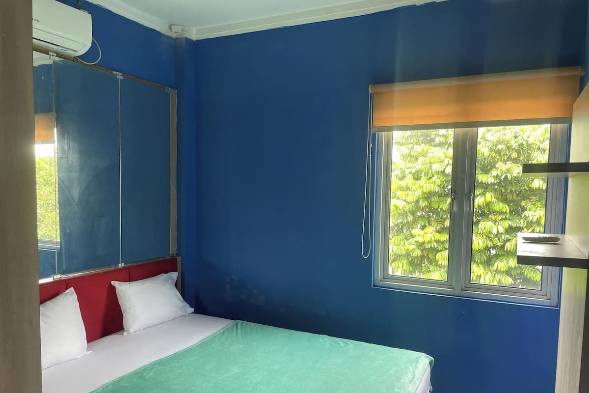 A room with a bed, a window with a view of trees, and an air conditioning unit.