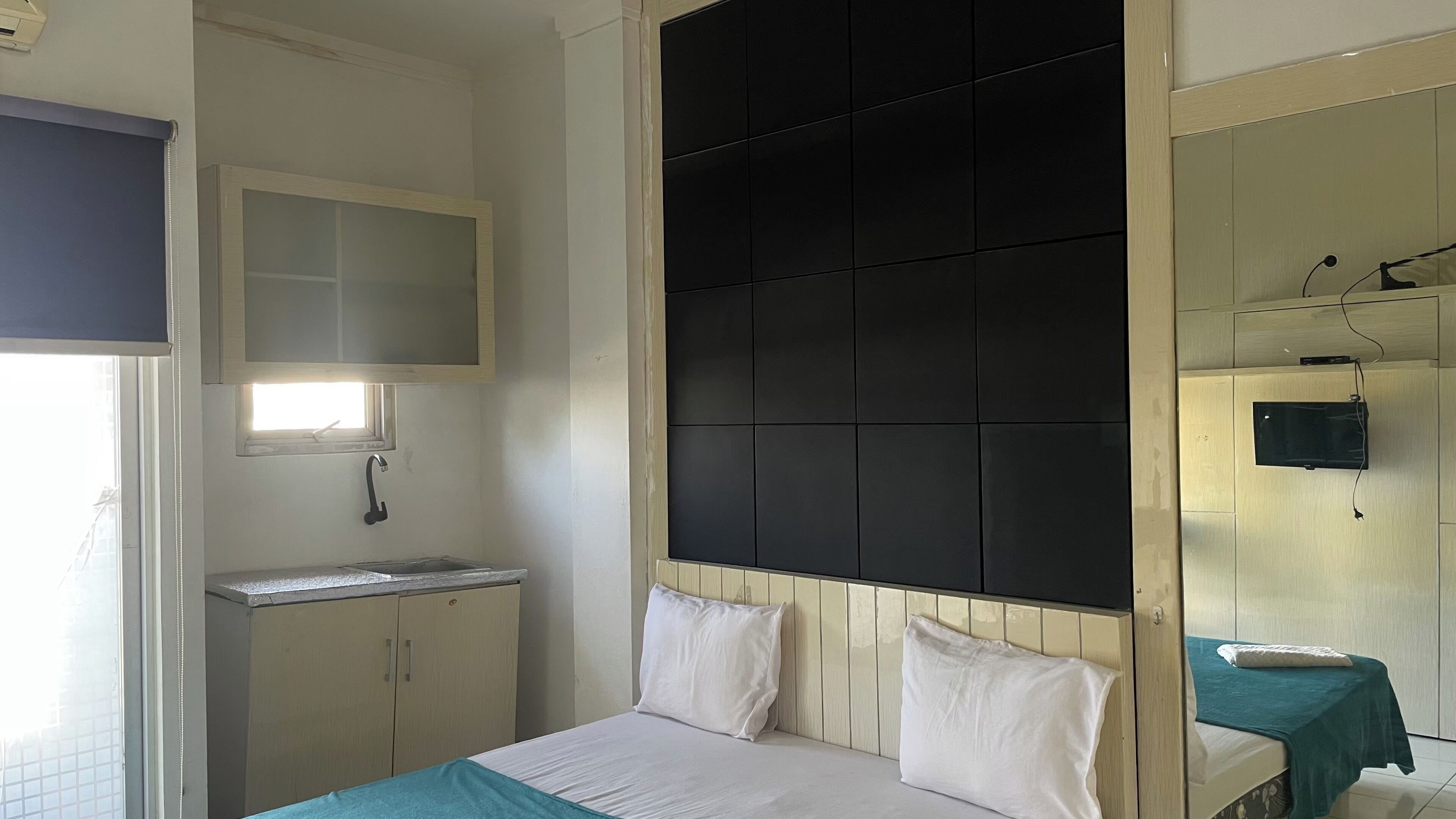 Une chambre à coucher avec un lit, une petite table de chevet, un miroir et un téléviseur fixé au mur.
