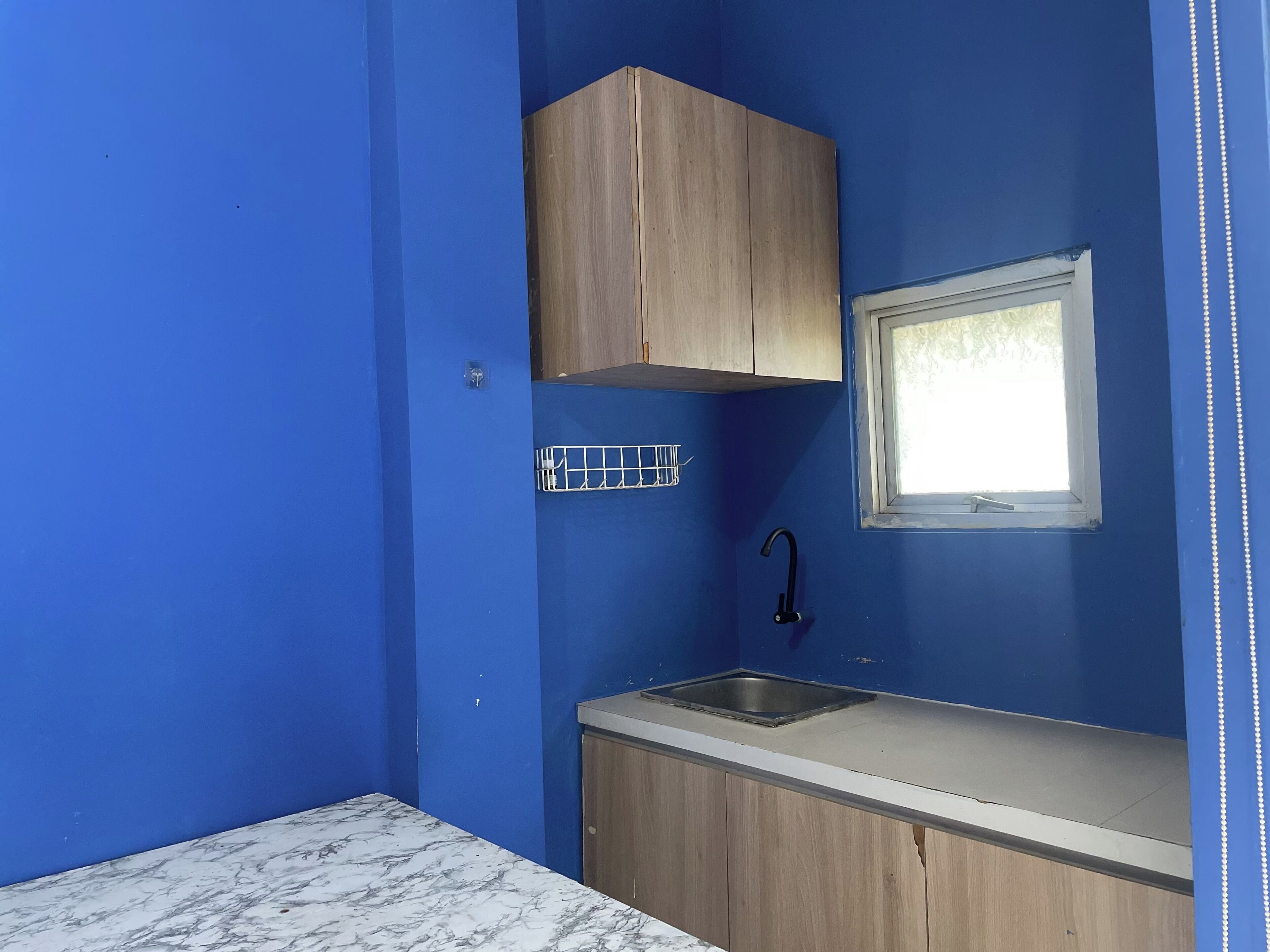 Eine kleine Küchenzeile mit blauen Wänden, einem Holzkorpus, einem Spülbecken und einem Fenster.