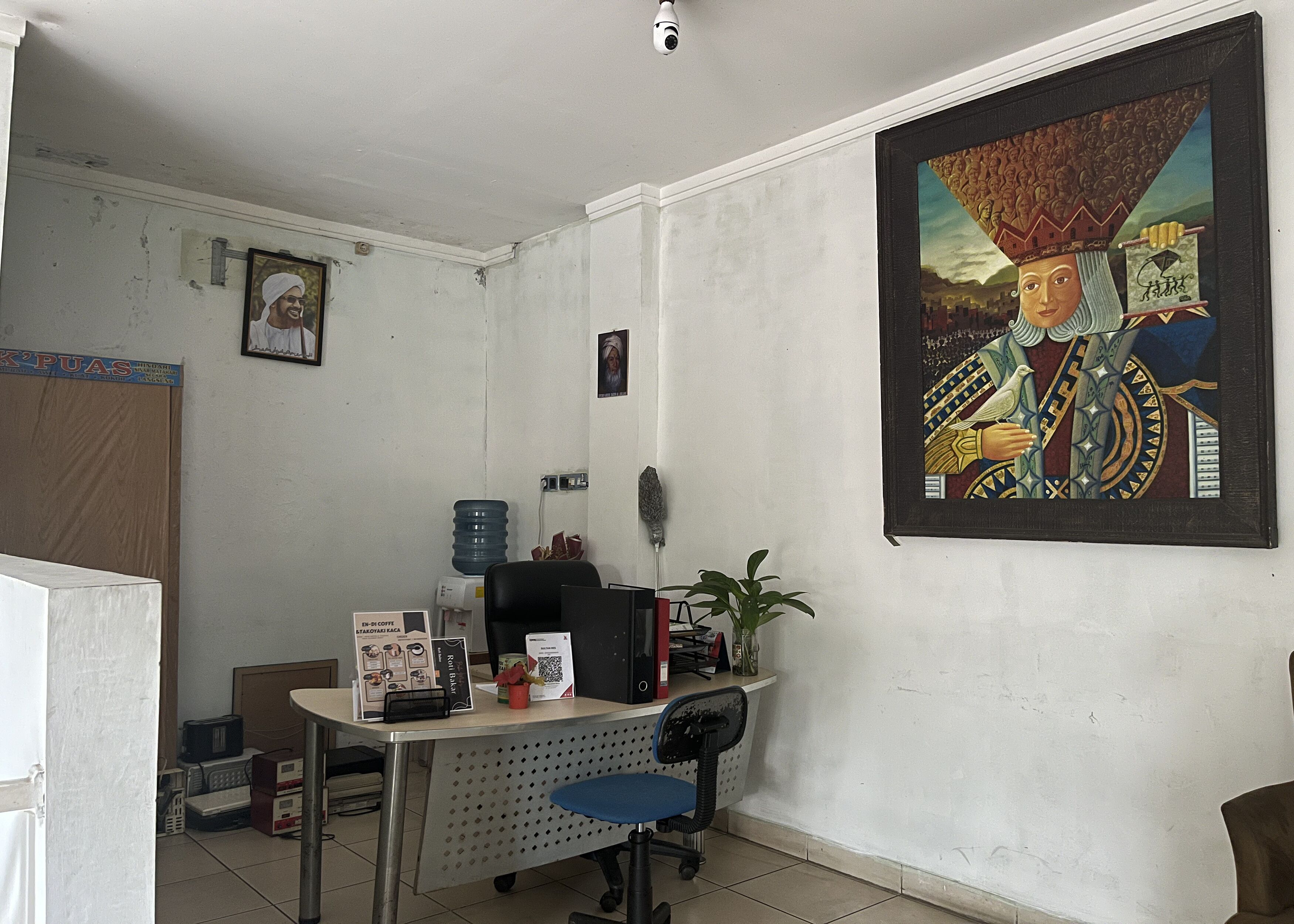 A room with a desk, chair, and a large painting on the wall.