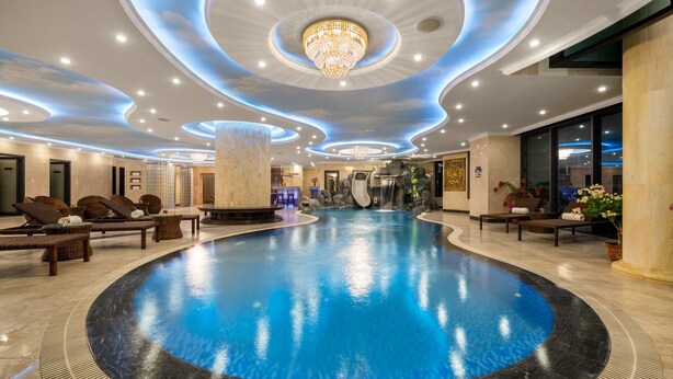 Amplia zona de piscina interior con una fuente central, rodeada de sillones de descanso y un moderno diseño de techo.