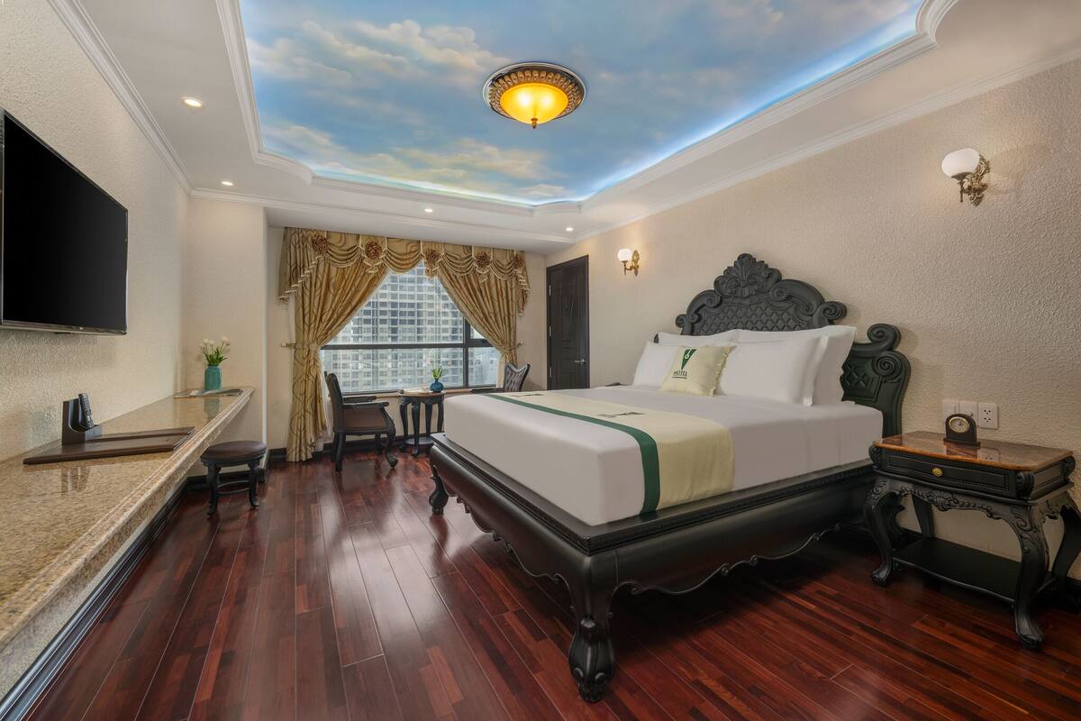 A hotel room with a bed, a TV, a desk, and a window with curtains.