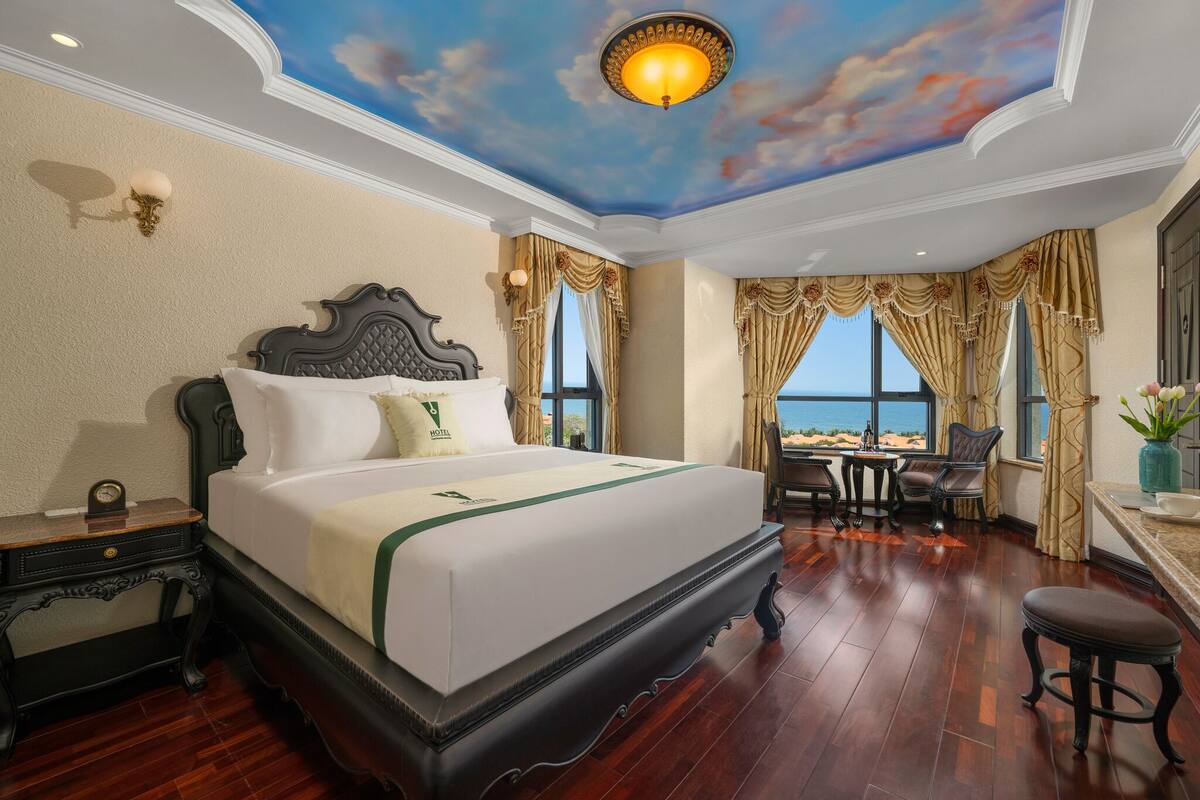 A hotel room with a large bed, a desk, and a view of the beach.