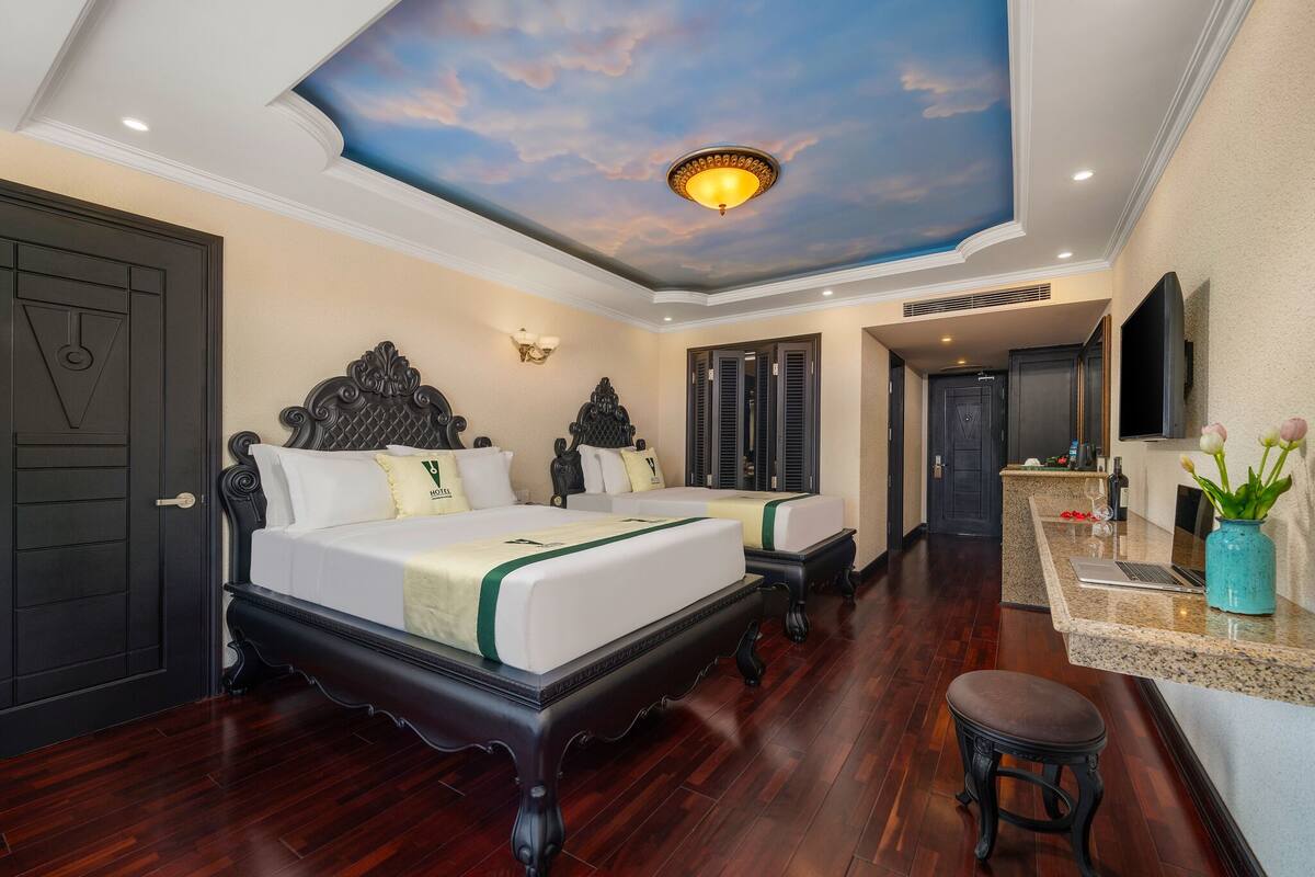 A hotel room with a large bed, a desk, and a ceiling mural.