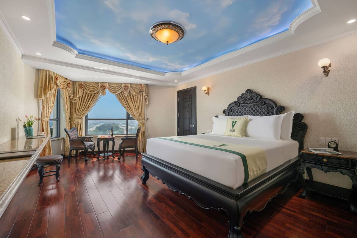 A hotel room with a large bed, a desk, a chair, and a view of the city.