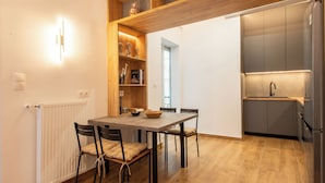 A modern kitchen with a built-in oven, a wooden dining table with chairs, and a shelf with decorative items.