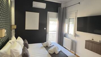A modern hotel room with a large bed, a flat-screen TV, a built-in air conditioning unit, and a view of the outdoors.