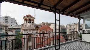 A balcony with patterned flooring, a view of a building with a bell tower, and a metal railing.