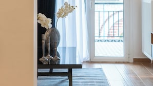 A hallway with a dark curtain, a vase with white flowers, and a view of a balcony with a railing.