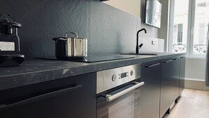 A modern kitchen with a black countertop, stainless steel appliances, and a large window. - Alfred Suites (Dijon)