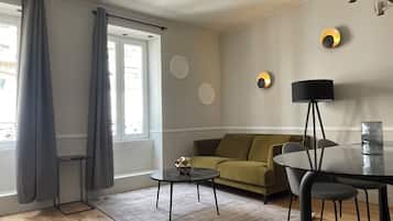 Uma sala de estar moderna com sofá, mesa de centro, mesa de jantar com cadeiras, abajur e janela com cortinas.