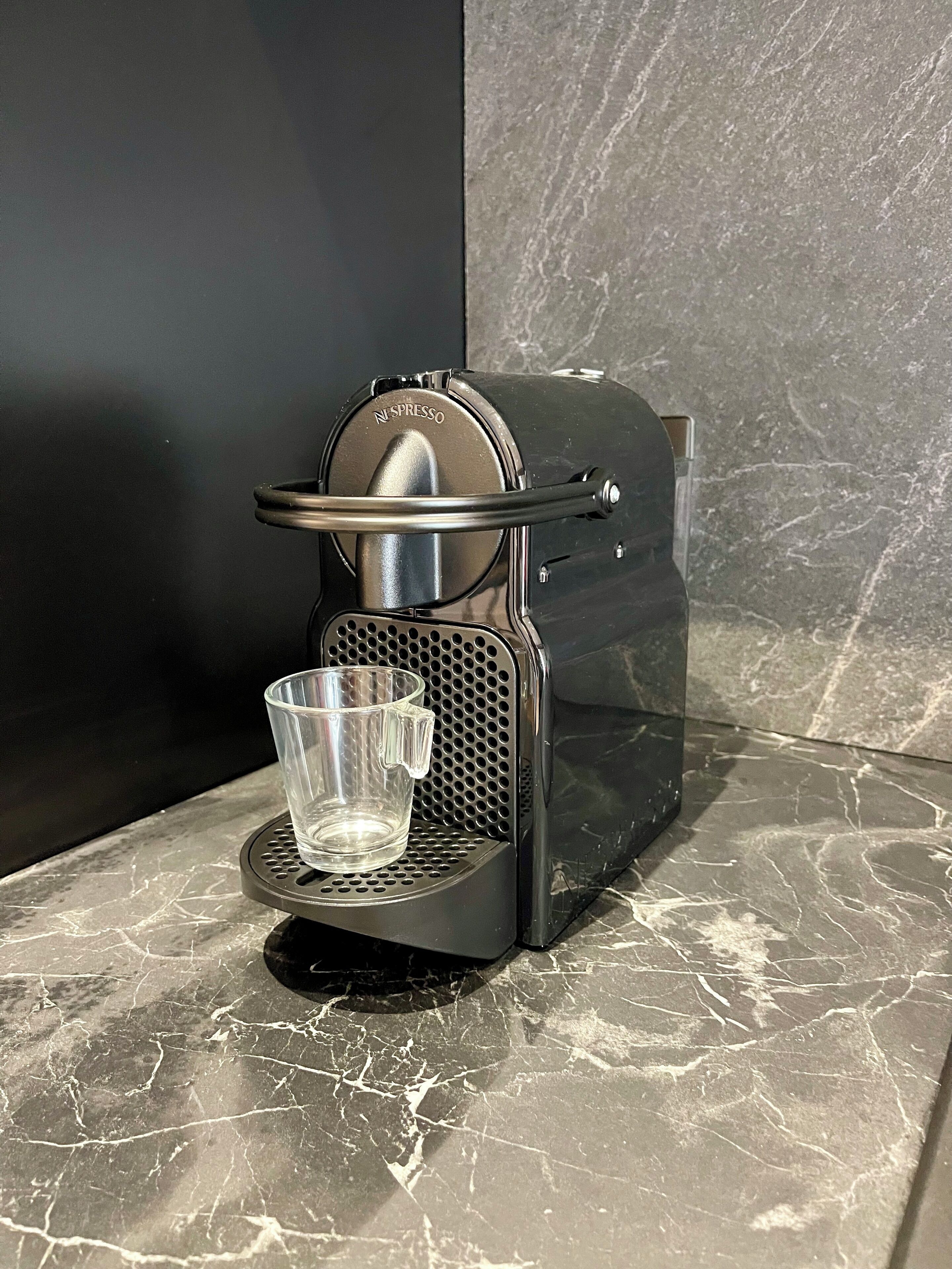 Une machine à café Nespresso avec une tasse en verre transparent posée sur le bac d’égouttement, elle-même placée sur un comptoir en marbre.