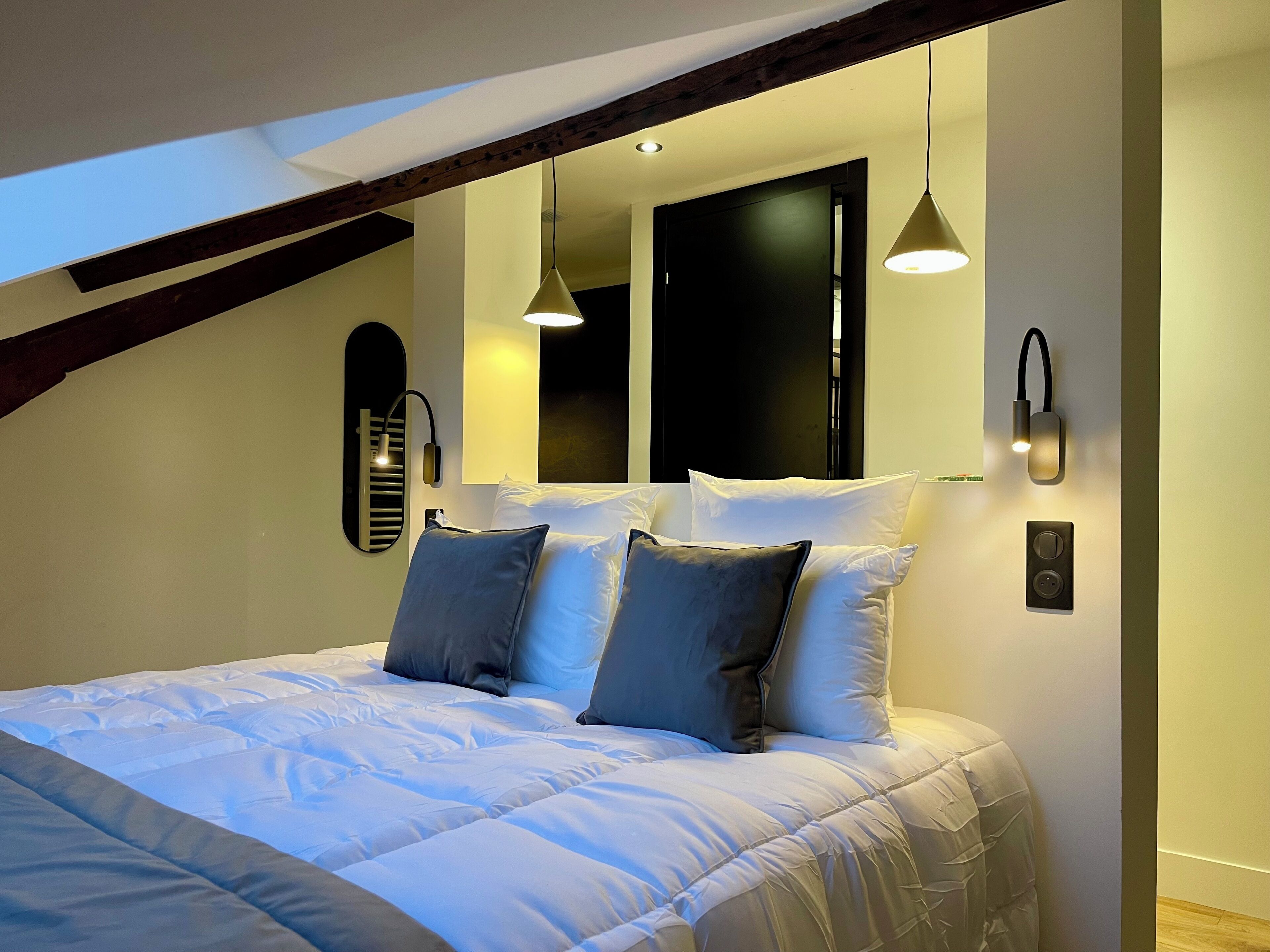 A modern bedroom with a large bed, two wall-mounted lights, and a skylight.