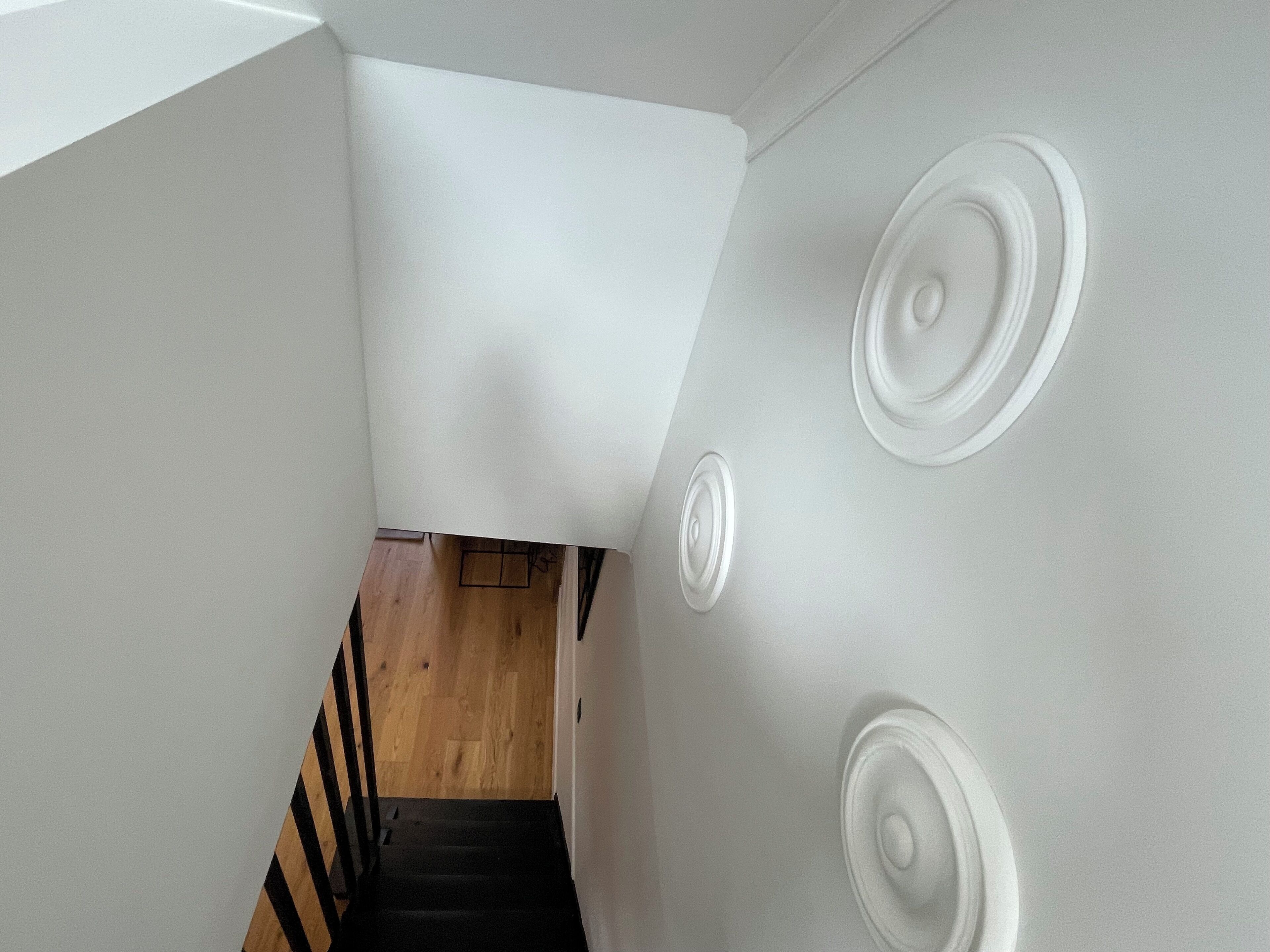Una escalera de madera con barandillas negras que lleva a un rellano con pared blanca y adornos circulares en la pared.