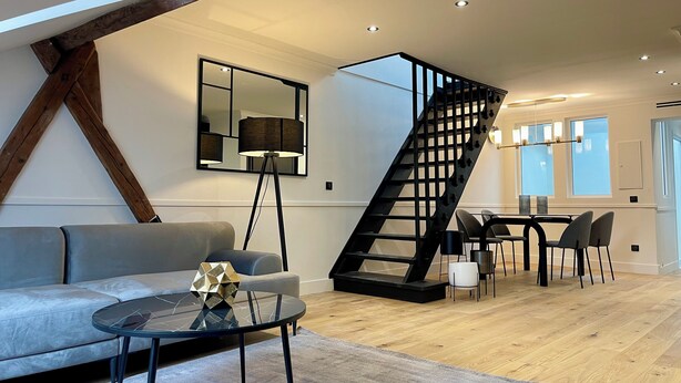 A modern living room with a sofa, coffee table, and a black spiral staircase. - Alfred Suites (Dijon)