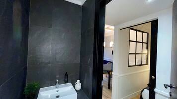 A modern bathroom with a dark tiled wall, a white sink, and a small potted plant.