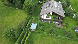 Vue aérienne d’une maison dotée d’un toit en pente, entourée d’un jardin bien entretenu et d’un vignoble.